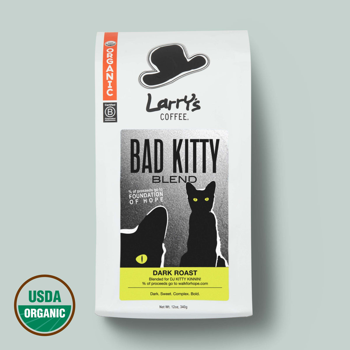 A 12 oz bag of Larry's Coffee 'Bad Kitty' Blend Dark Roast, featuring a white bag with black graphics of a hat and cat, a yellow label accent, and a USDA Organic seal in the bottom left corner, set against a solid sage green background.