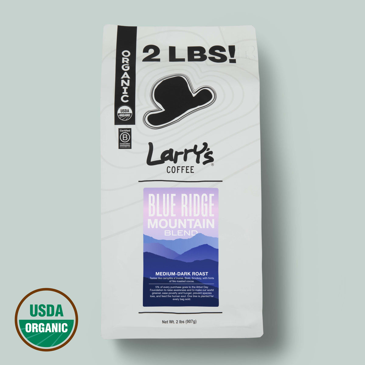 A 2 lb bag of Larry's Coffee Blue Ridge Mountain Blend medium-dark roast, featuring a white bag with a black hat logo and a purple mountain graphic, shown on a light gray-green background with a USDA Organic seal in the lower left corner.