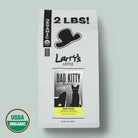 A 2 lb bag of Larry's Coffee 'Bad Kitty' Blend Dark Roast, featuring a white bag with black graphics of a hat and cat, a yellow label accent, and a USDA Organic seal in the bottom left corner, set against a solid sage green background.