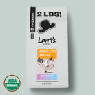 A 2 lb bag of Larry's Coffee 'Magic City Decaf' on a light sage green background, featuring a white bag with black text and graphics, a USDA Organic seal, and a black cowboy hat logo.