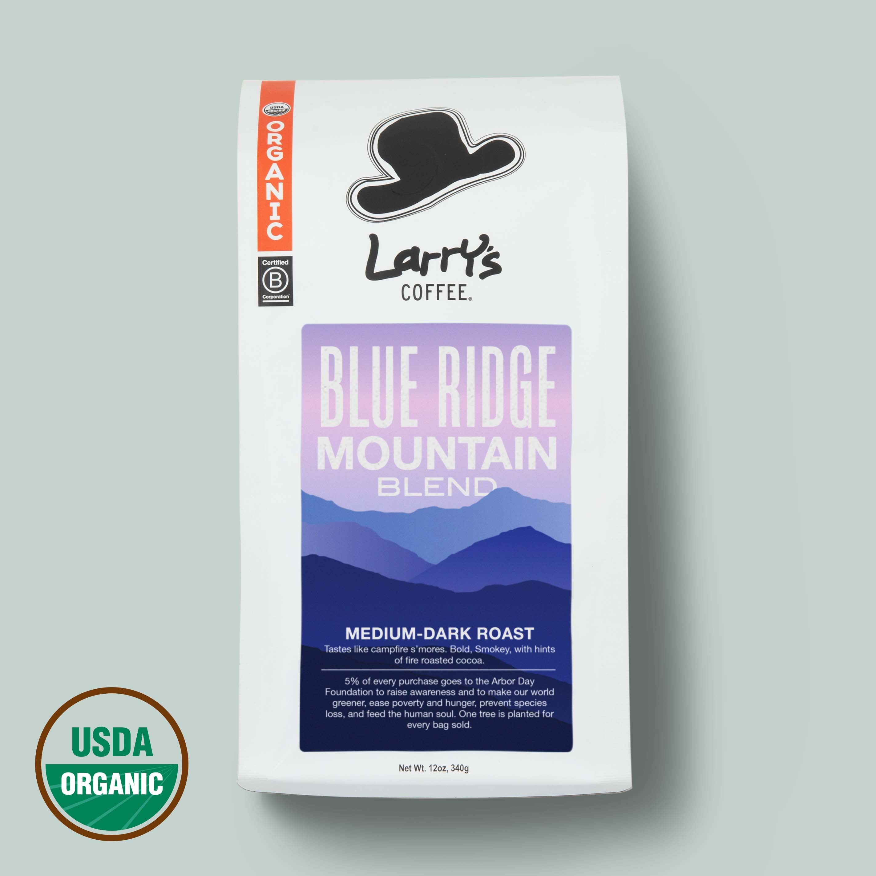 A bag of Larry's Coffee Blue Ridge Mountain Blend medium-dark roast coffee on a light gray background, featuring a white bag with a purple and blue label, a black cowboy hat logo, and a USDA Organic seal in the lower left corner.